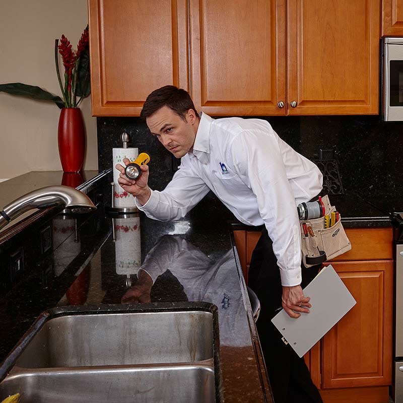 Technician scanning for bugs in a kitchen using a flashlight.